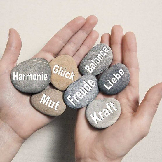 Hände halten Steine mit Glück, Mut, Kraft, Freude, Harmonie